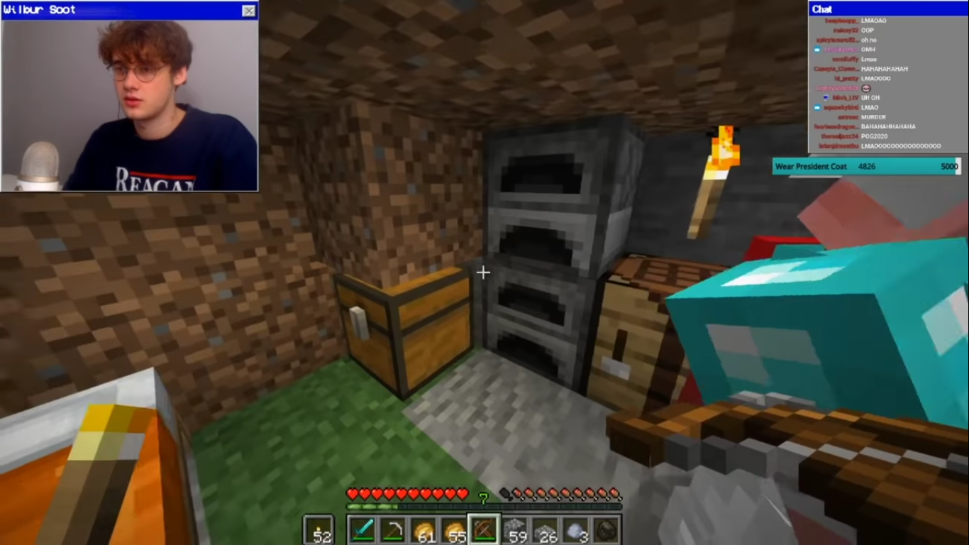 A screenshot from Wilbur's stream. It shows a very basic dirt house that one might build on their first day on a minecraft world. In the screenshot, there is a bed, two furnaces, a chest, and a crafting table. Wilbur holds a torch in his offhand and a crossbow in his dominant hand.